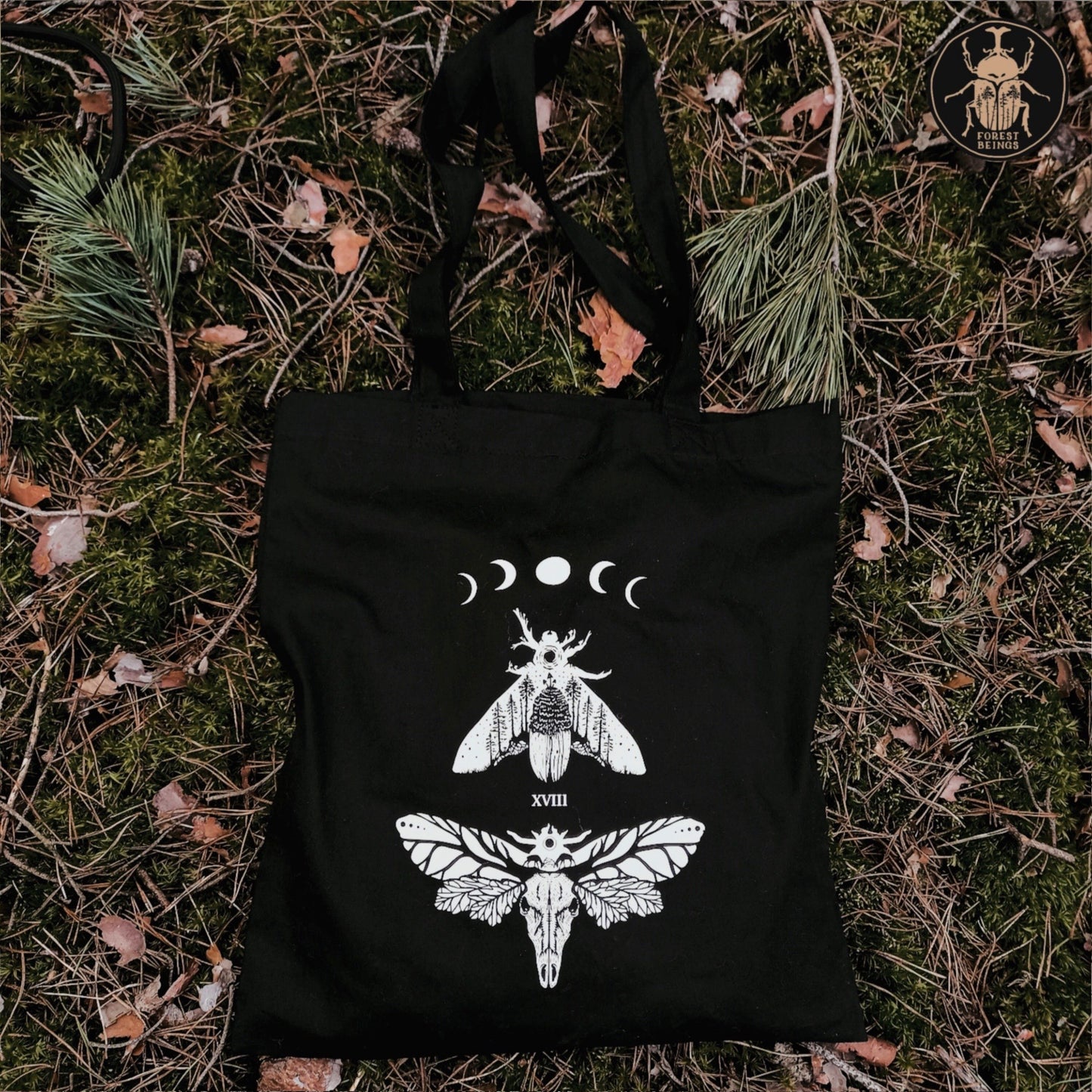 A gothic tote bag laying on the ground in the forest.
