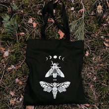 Load image into Gallery viewer, A gothic tote bag laying on the ground in the forest.
