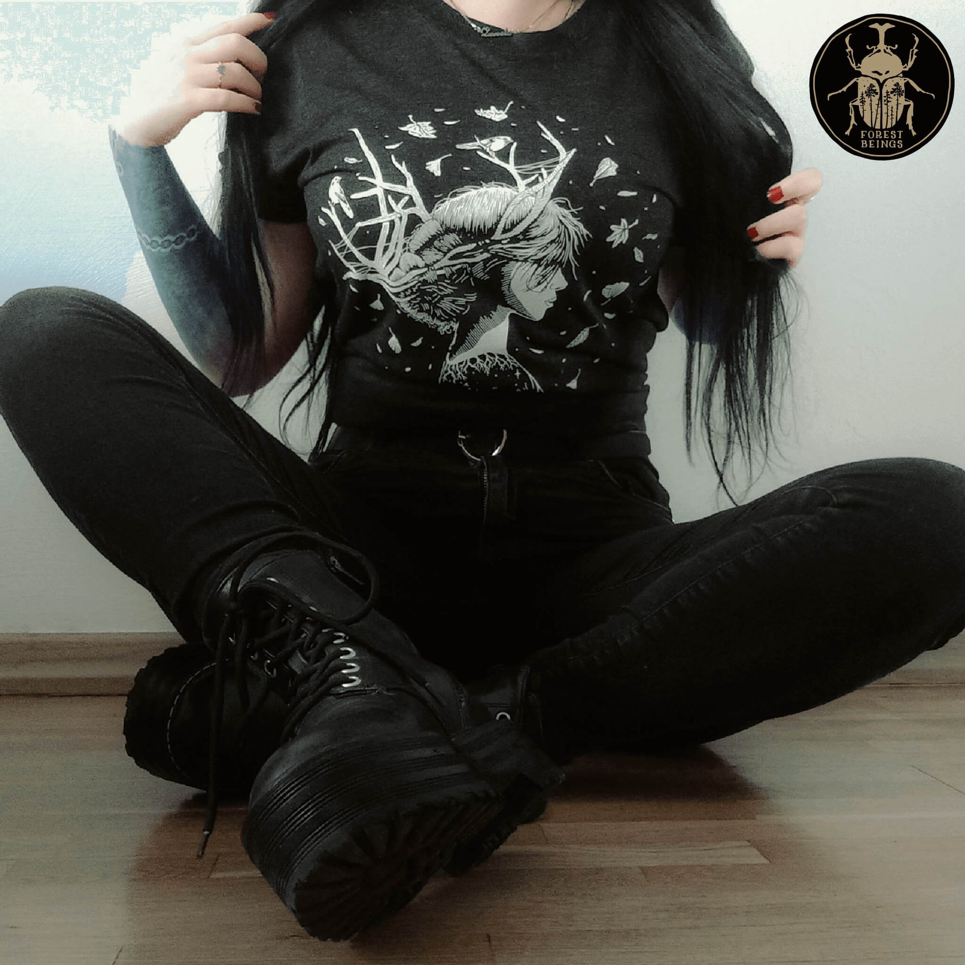 Gothic girl with tattoos and wearing all black. The outfit is a soft goth aesthetic. She is wearing a witchy t-shirt.
