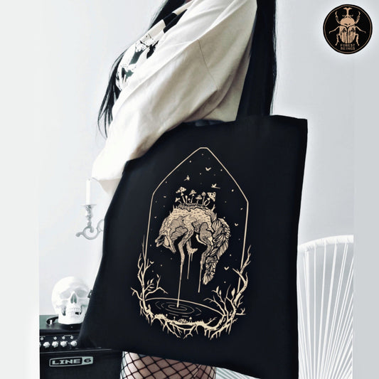 The dying fox and the mushrooms design on an aesthetic gothic black tote bag worn by a gothic girl with fishnet stockings. 