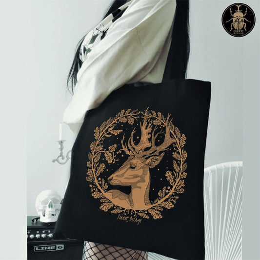 A gothic girl with fishnet stockings wearing an aesthetic gothic black tote bag with a golden deer print on it.