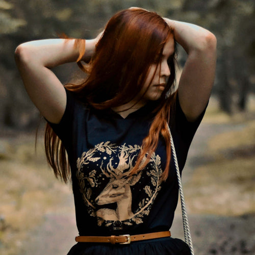 A beautiful redhead girl wearing a golden deer gothic t-shirt in the middle of the forest. 