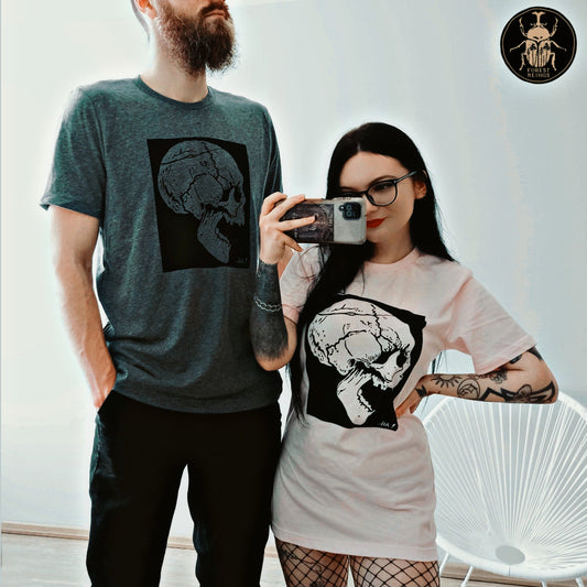 A cute gothic couple with tattoos wearing matching t-shirts. Both wearing a skull gothic shirts.