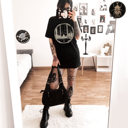 Cute witchy goth girl with long black hair and tattoos on her arms and legs, wearing an aesthetic goth graphic t-shirt. The print on the t-shirt is John Bauer's most famous illustration of Princess Tuvstarr.
