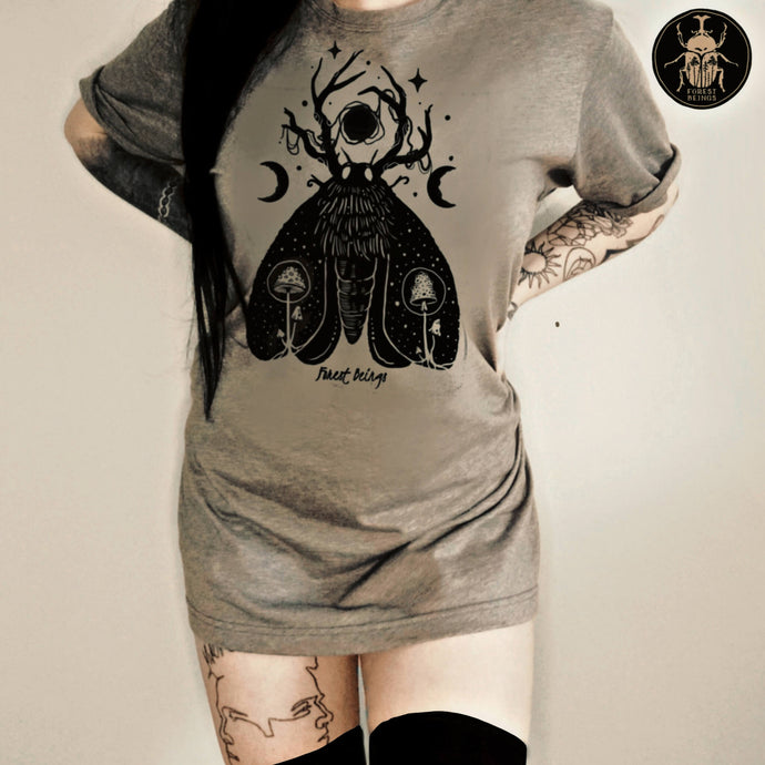  Cute witchy goth girl with long black hair and tattoos on her arms and legs, wearing an aesthetic goth graphic t-shirt. The design on the t-shirt is a black luna moth surrounded by two moons. Inside the moth there are two mushrooms.