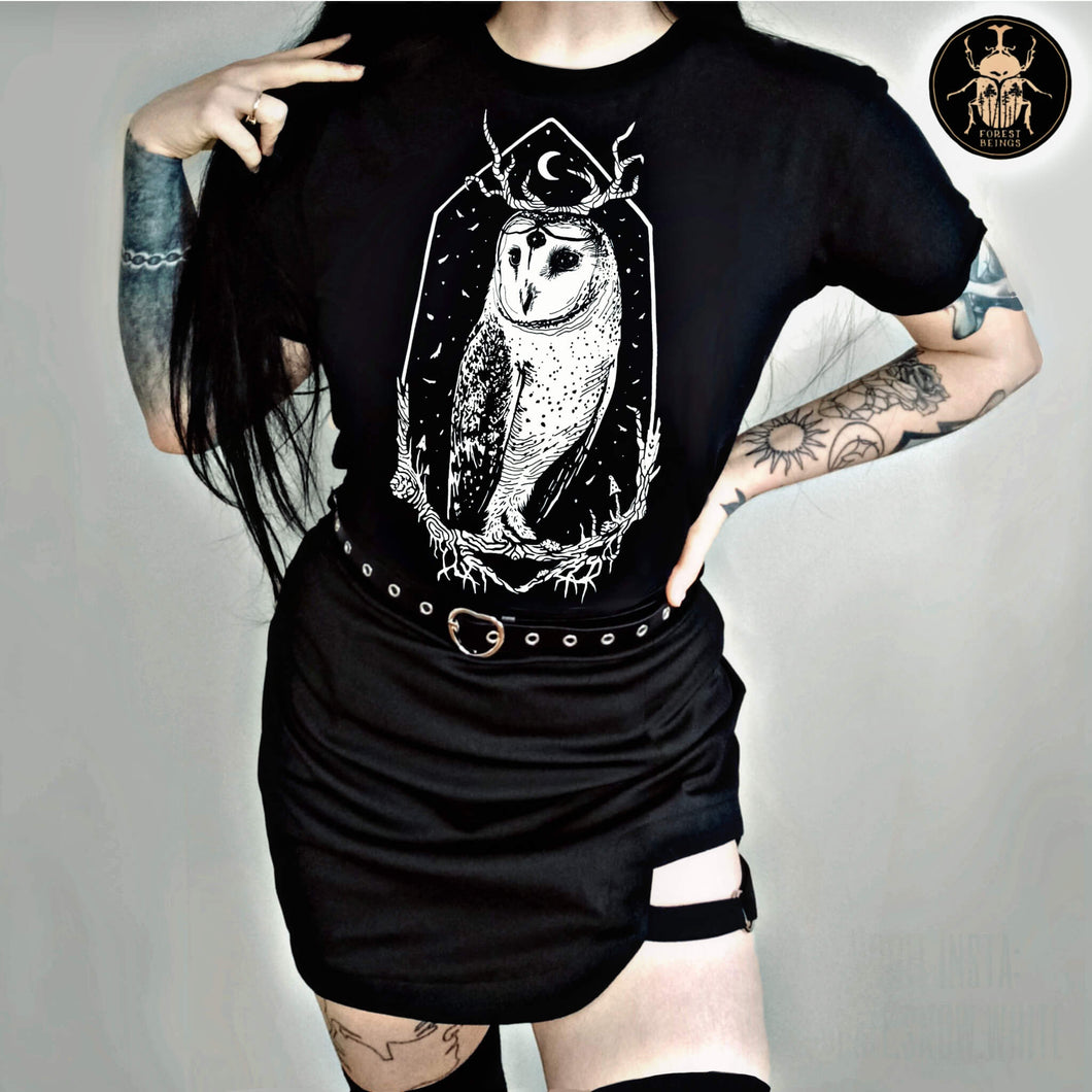  Cute witchy goth girl with long black hair and tattoos on her arms and legs, wearing an aesthetic goth graphic t-shirt. The print on the t-shirt is the barn owl Stolas . 