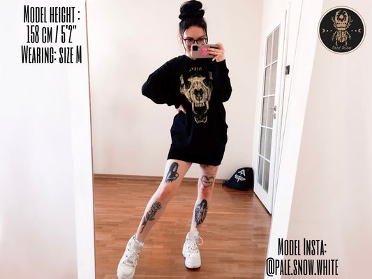 A cute gothic girl with a cool witchcore outfit.She is wearing a wolf skull viking witchy asthetic loose fit hoodie. The girl has many leg tattoos. 